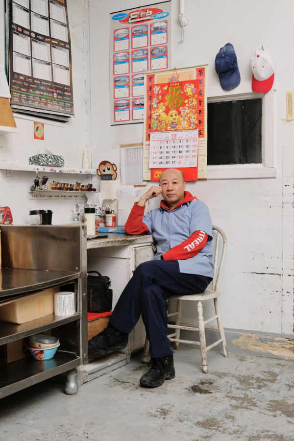 Employé de Wing assis devant un mur blanc décoré d'un calendrier chinois et de casquettes